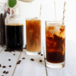 Proffee Made Easy: A Step-by-Step The Best Protein Coffee Recipe 3 A close-up of two tall glasses filled with iced Protein Coffee Recipe, one being swirled with cream, on a white wooden table